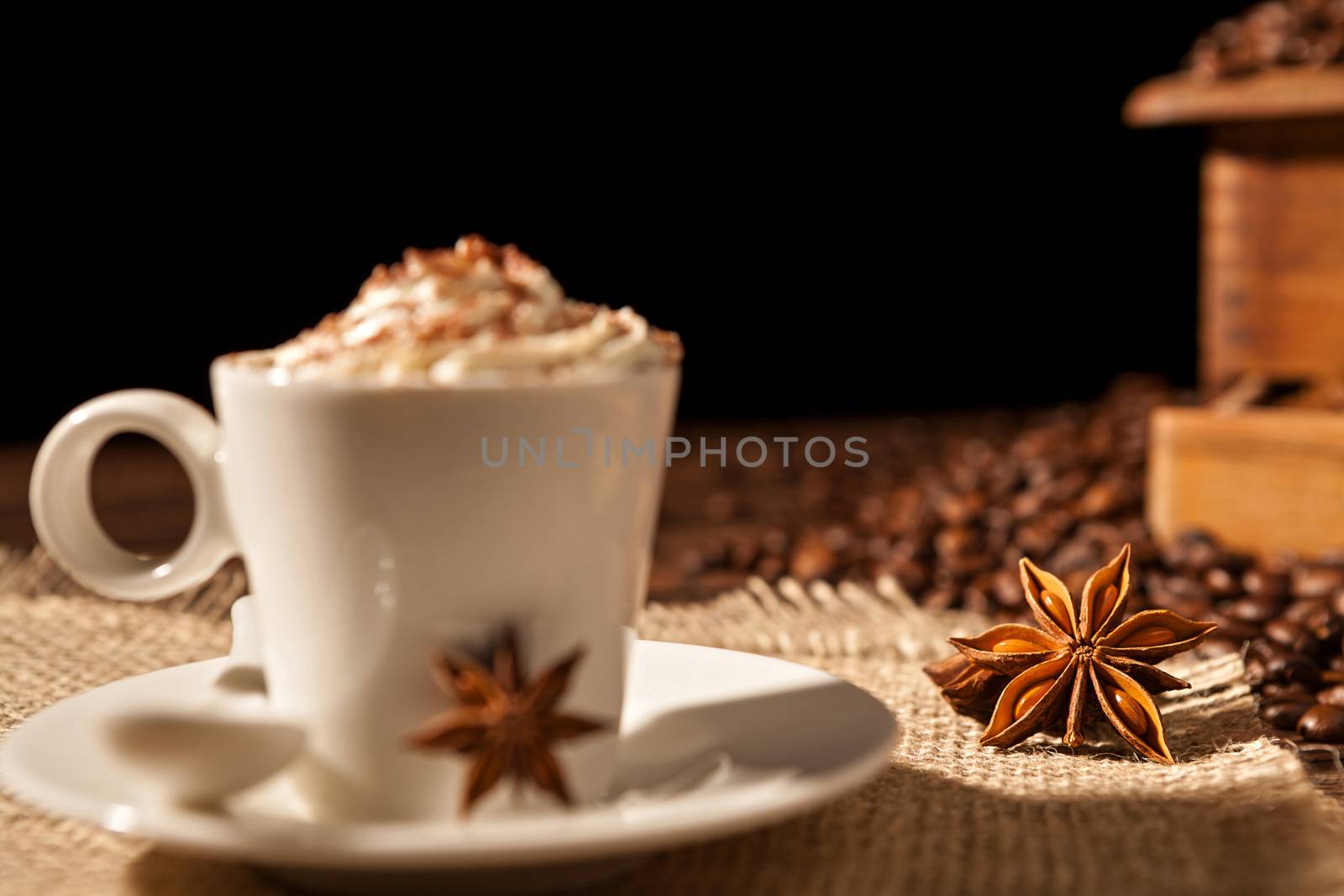 Close-up of coffee cup with whipped cream and star anise on a black background