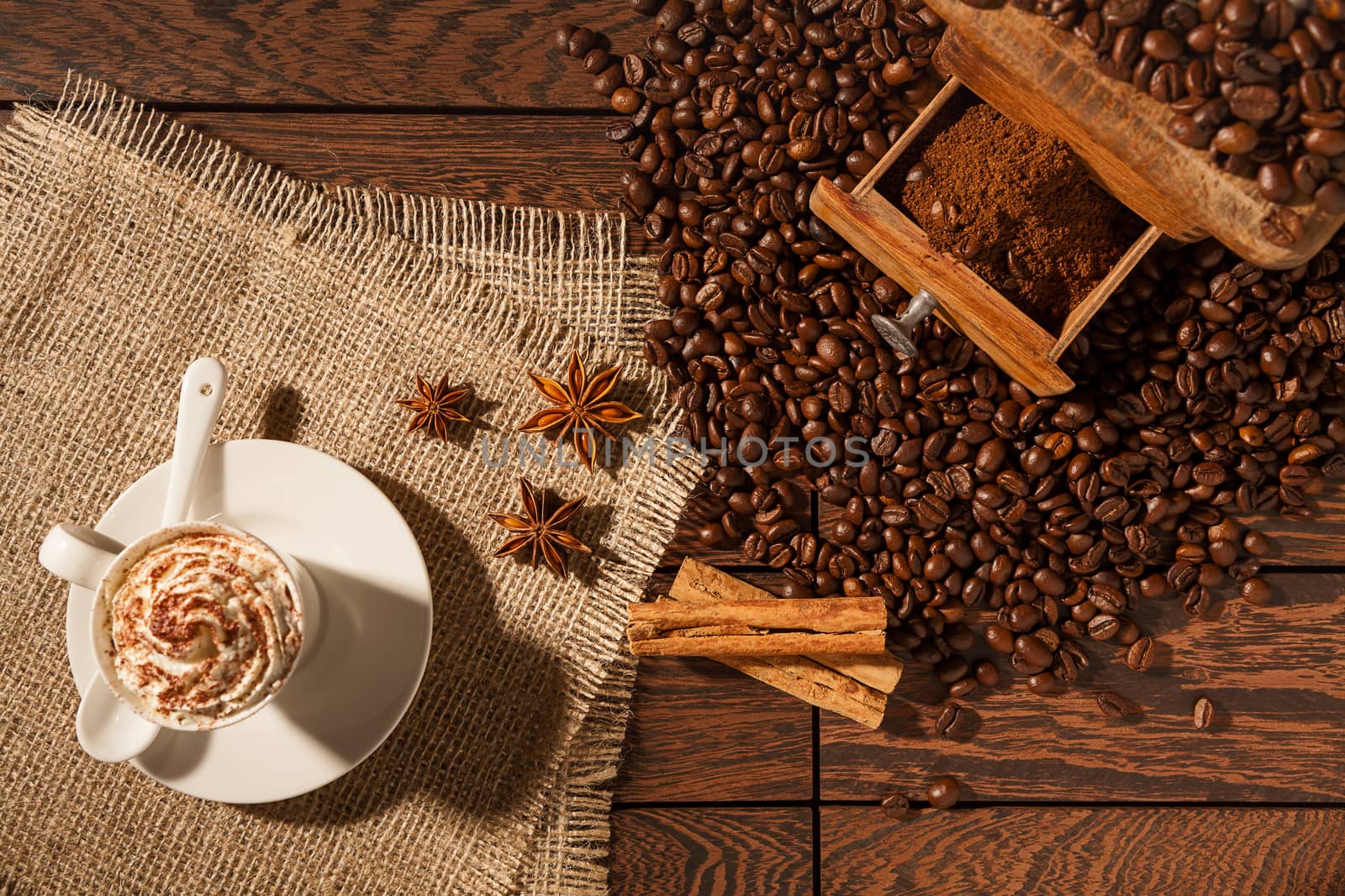 Coffee cup, star anise, cinnamon sticks and coffee beans seen from above