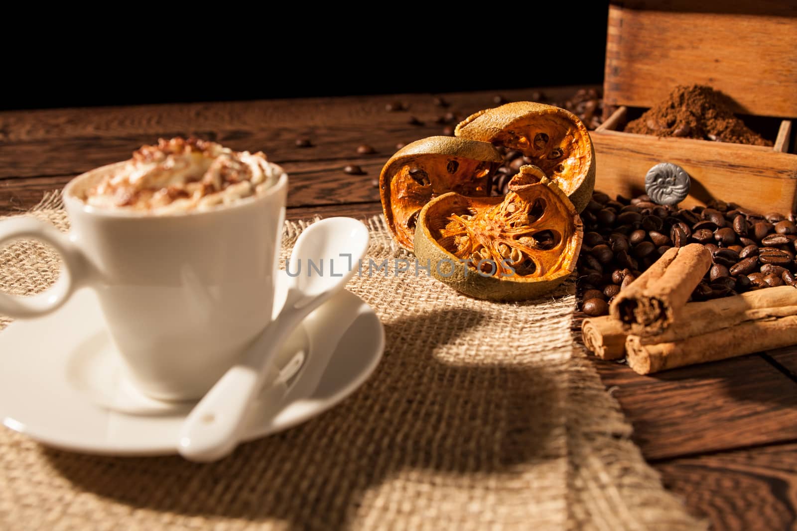Close-up of coffee cup, dried orange fruit and cinnamon sticks over a wooden background