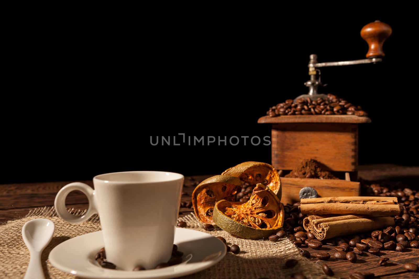 Coffee cup, dried orange fruit, cinnamon and coffee grinder on a black background
