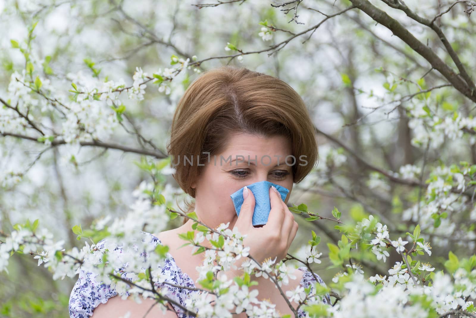 Woman with allergic rhinitis in  spring garden by olgavolodina