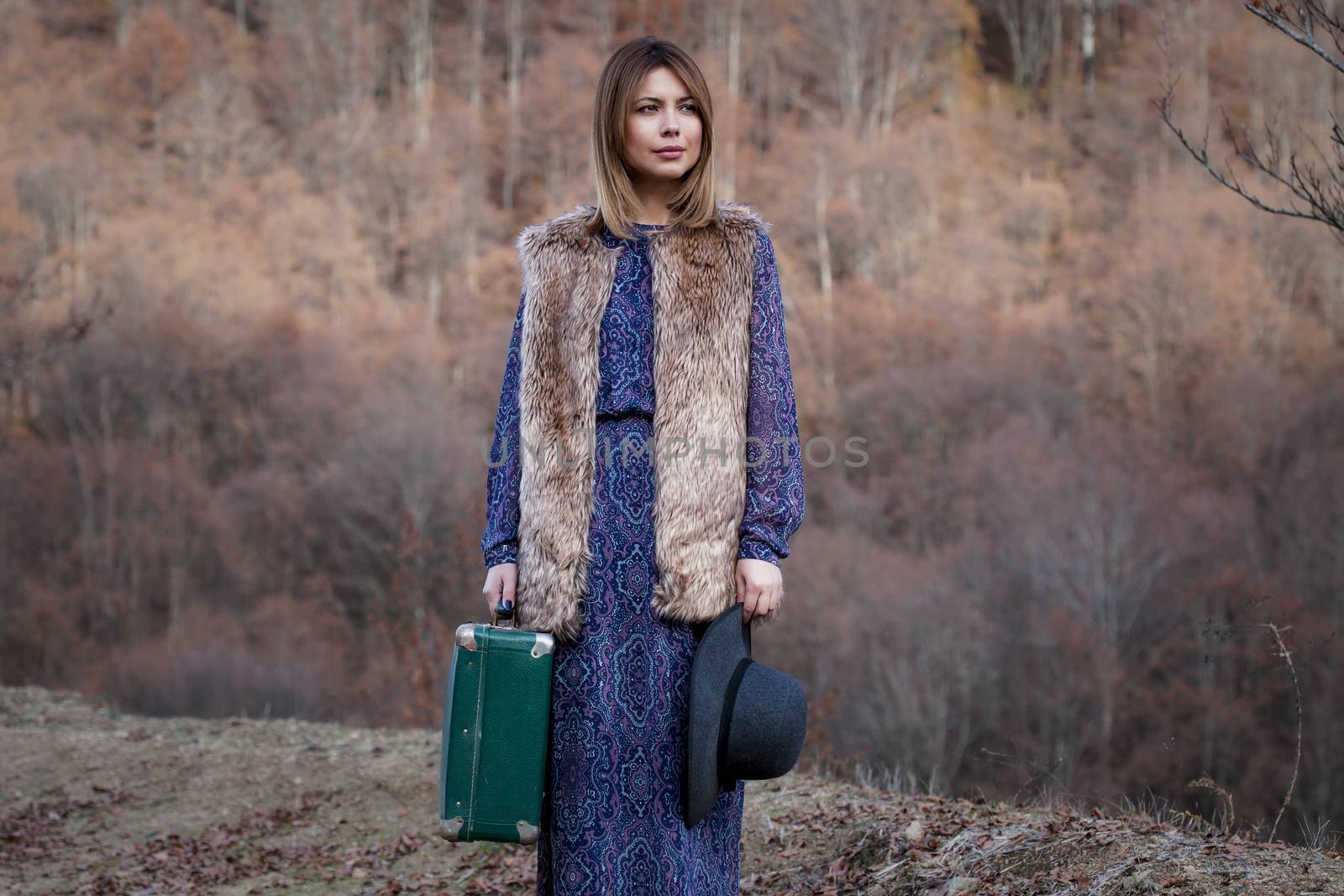 pretty young woman with a leather suitcase on a dirtroad in the mountains, vintage style