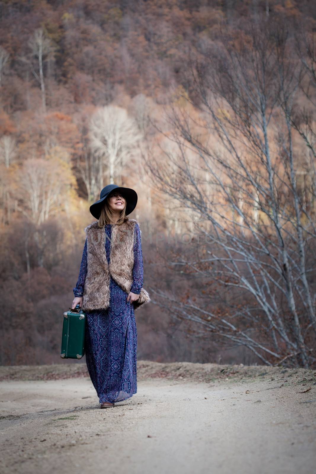 pretty young woman with a leather suitcase on a dirtroad in the mountains, vintage style