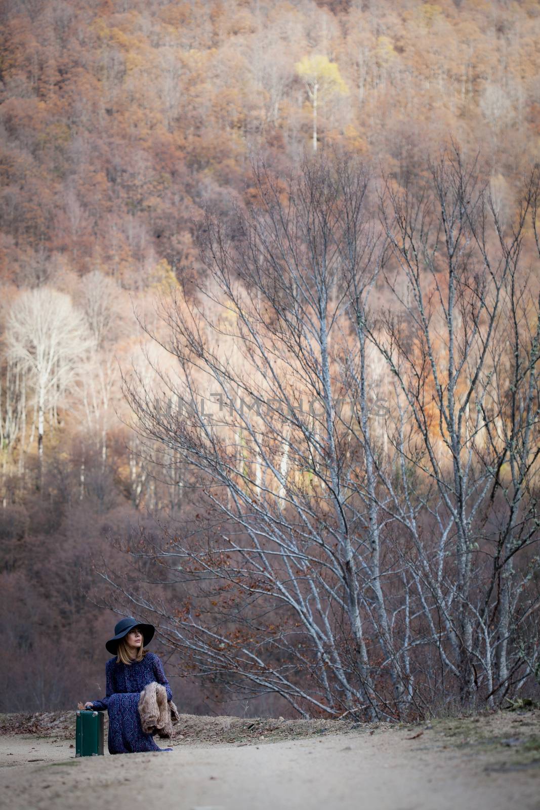 pretty young woman with a leather suitcase on a dirtroad in the mountains, vintage style