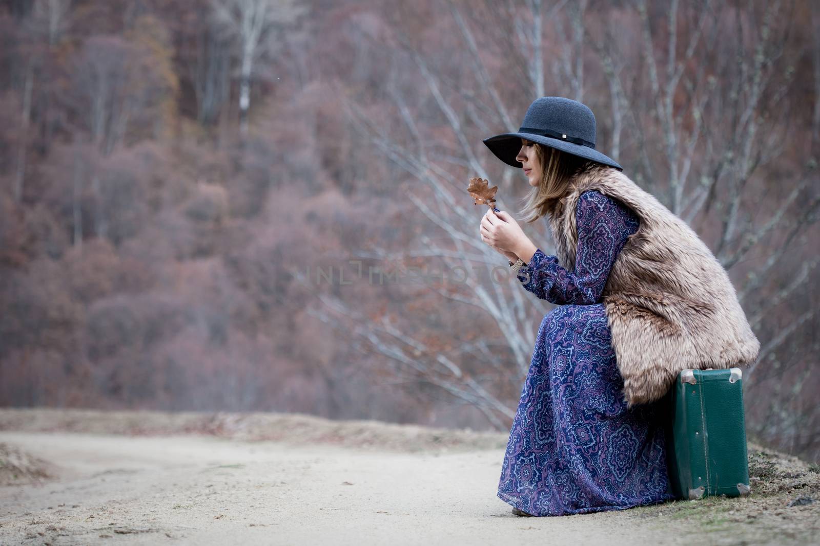 pretty young woman with a leather suitcase on a dirtroad in the mountains, vintage style