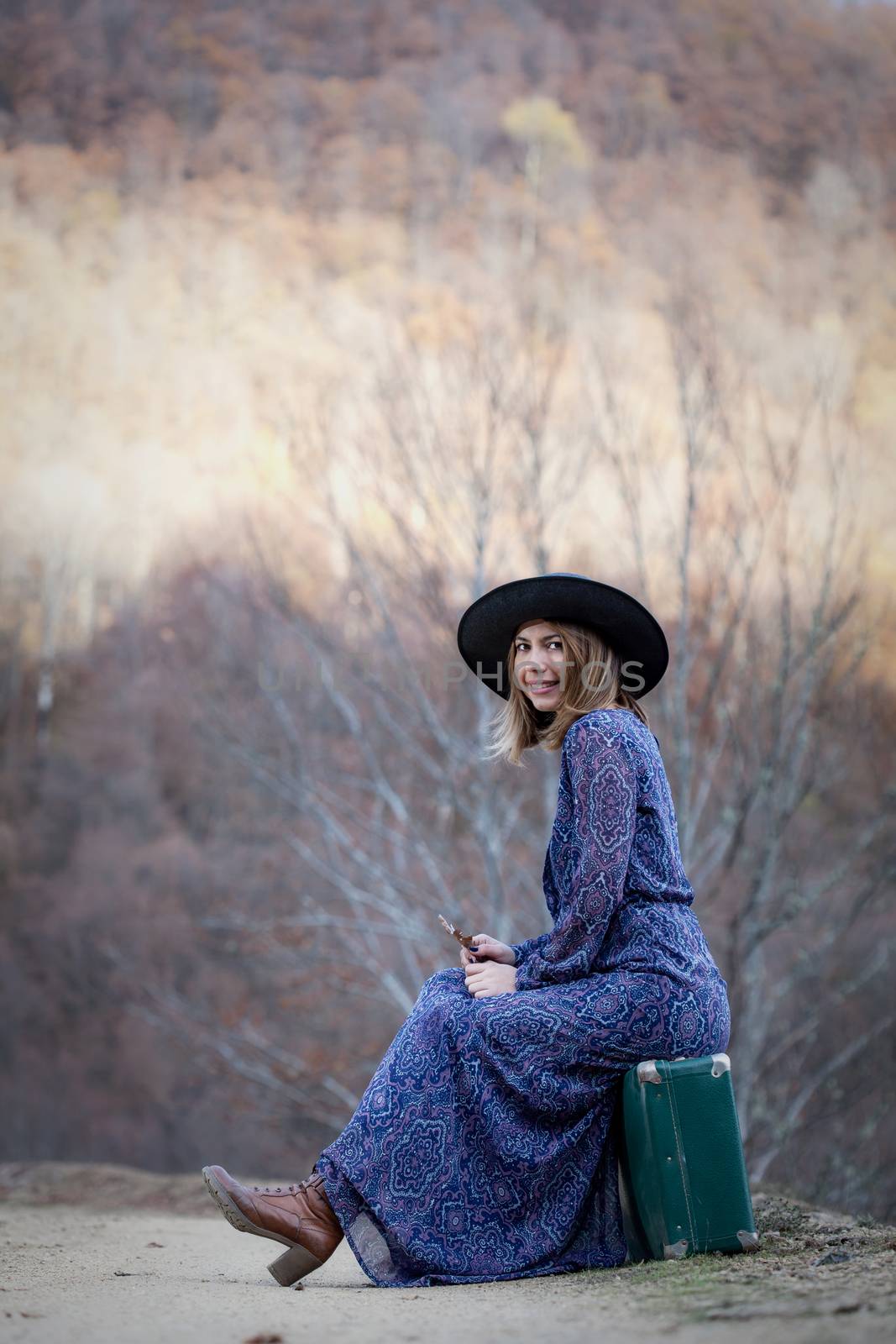 pretty young woman with a leather suitcase on a dirtroad in the mountains, vintage style