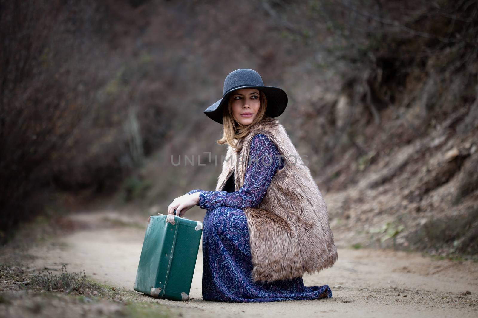 pretty young woman with a leather suitcase on a dirtroad in the mountains, vintage style