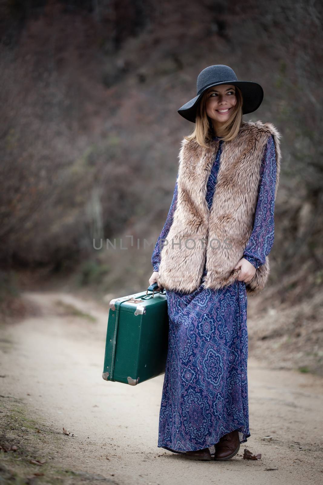 pretty young woman with a leather suitcase on a dirtroad in the mountains, vintage style