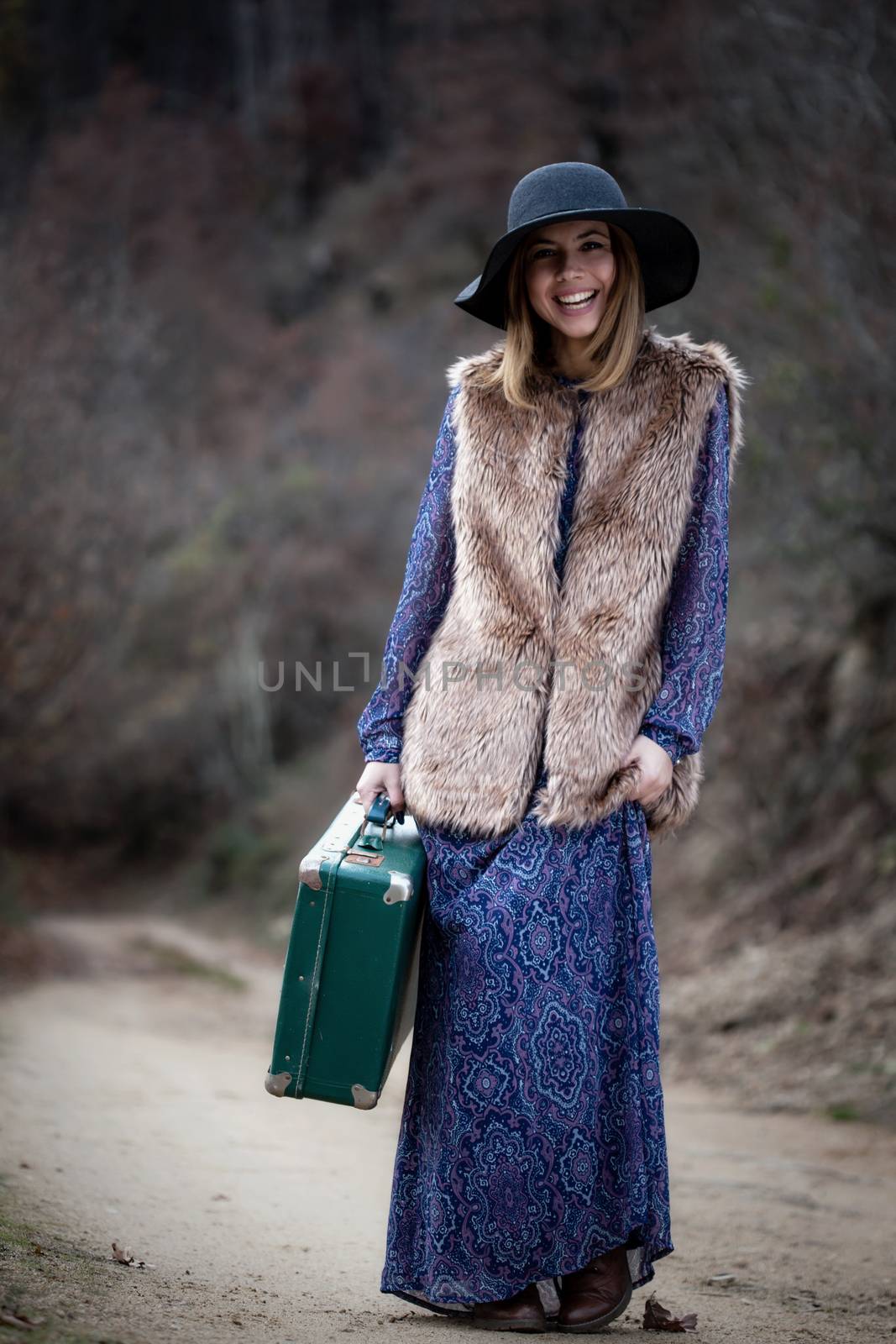 pretty young woman with a leather suitcase on a dirtroad in the mountains, vintage style