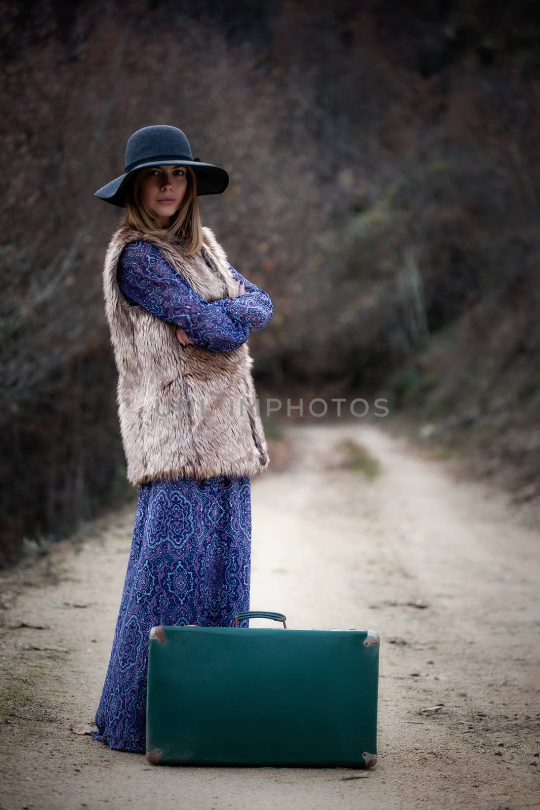 pretty young woman with a leather suitcase on a dirtroad in the mountains, vintage style