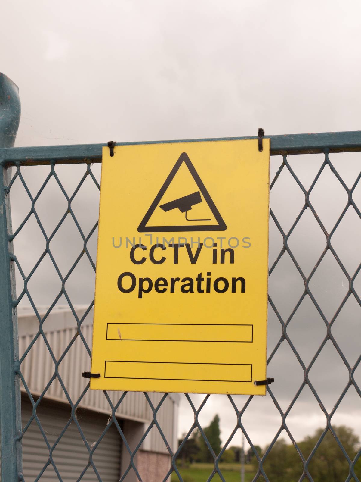yellow sign on fence saying cctv in operation outside
