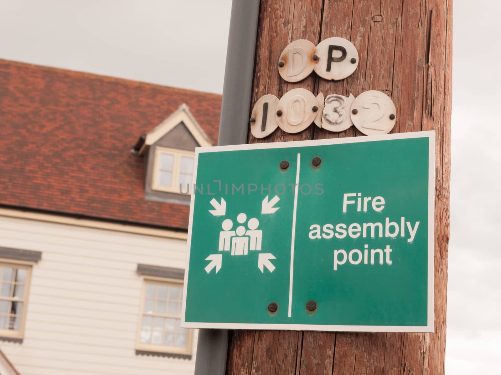 a green sign outside on a wooden pole saying fire assembly point fire warning