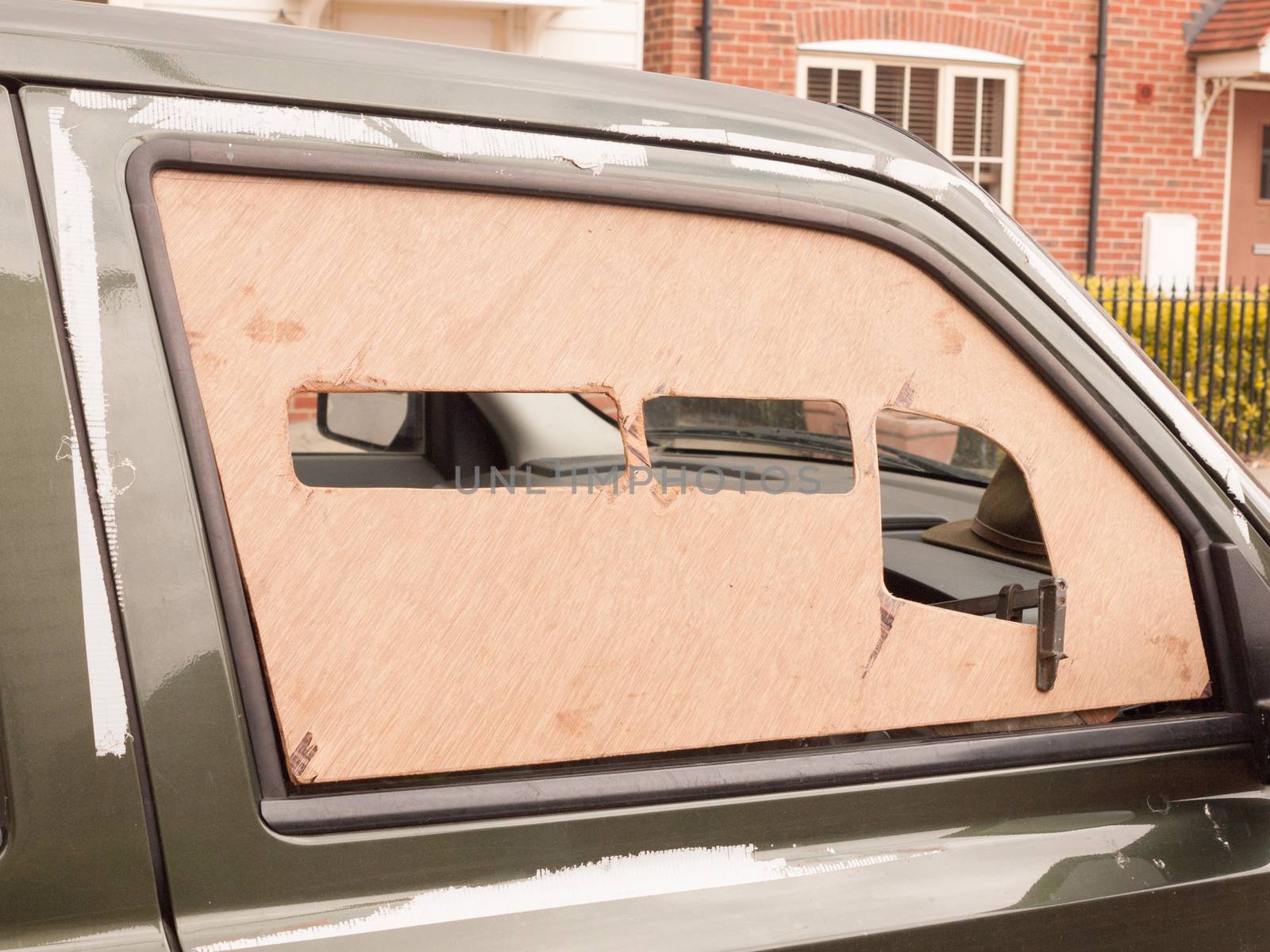 a car window boarded up with wood panel outside broken