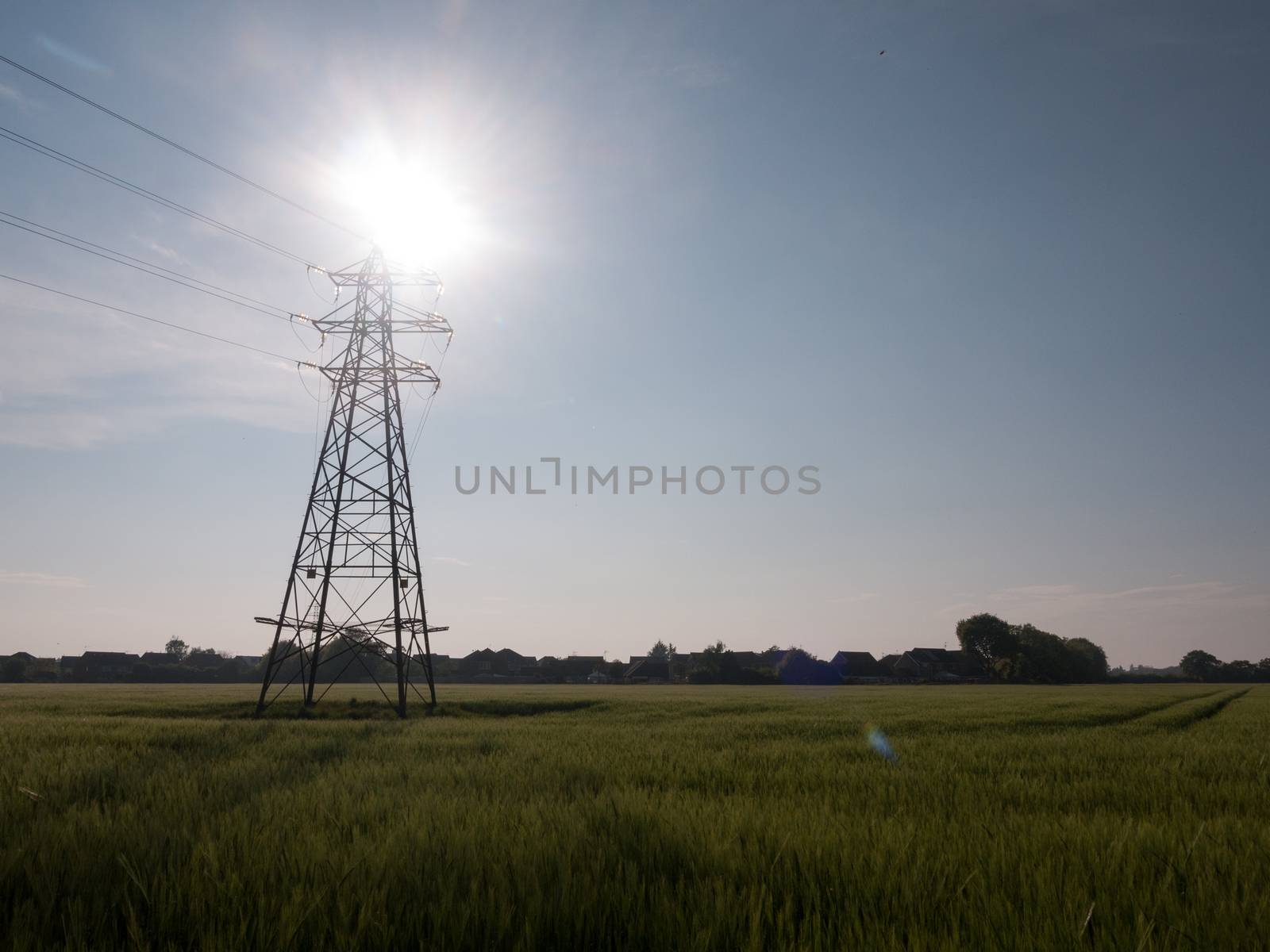 an electric pylon outside with sun behind it over field communication spring day