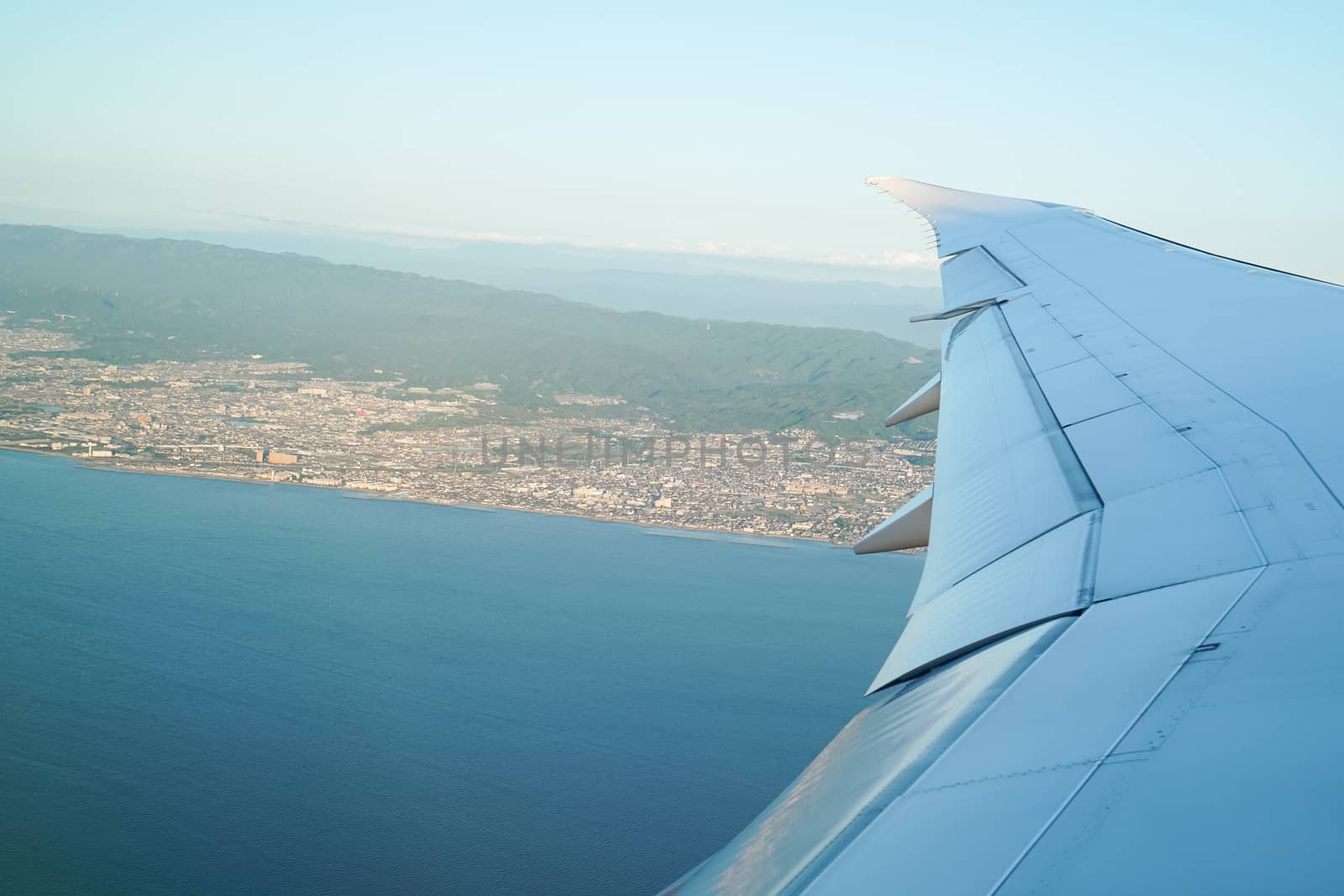 wing of an airplane flying above city and sea