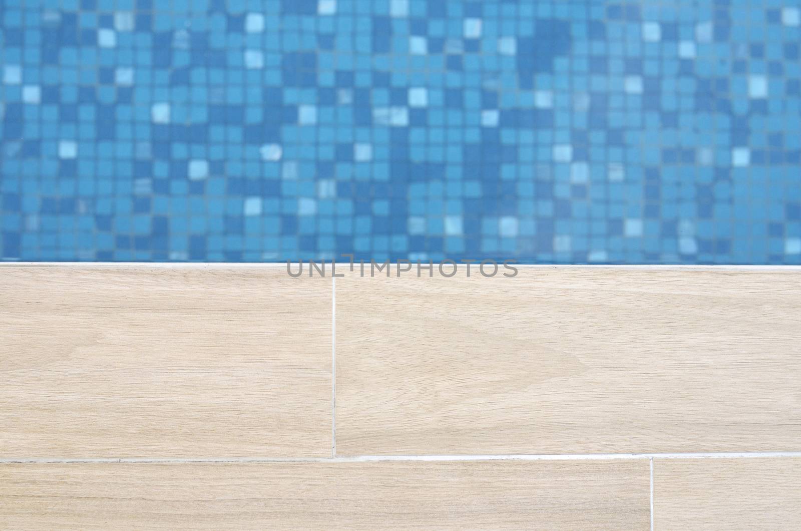 Close focus of edge of artificial wood floor near swimming pool with moving blue water