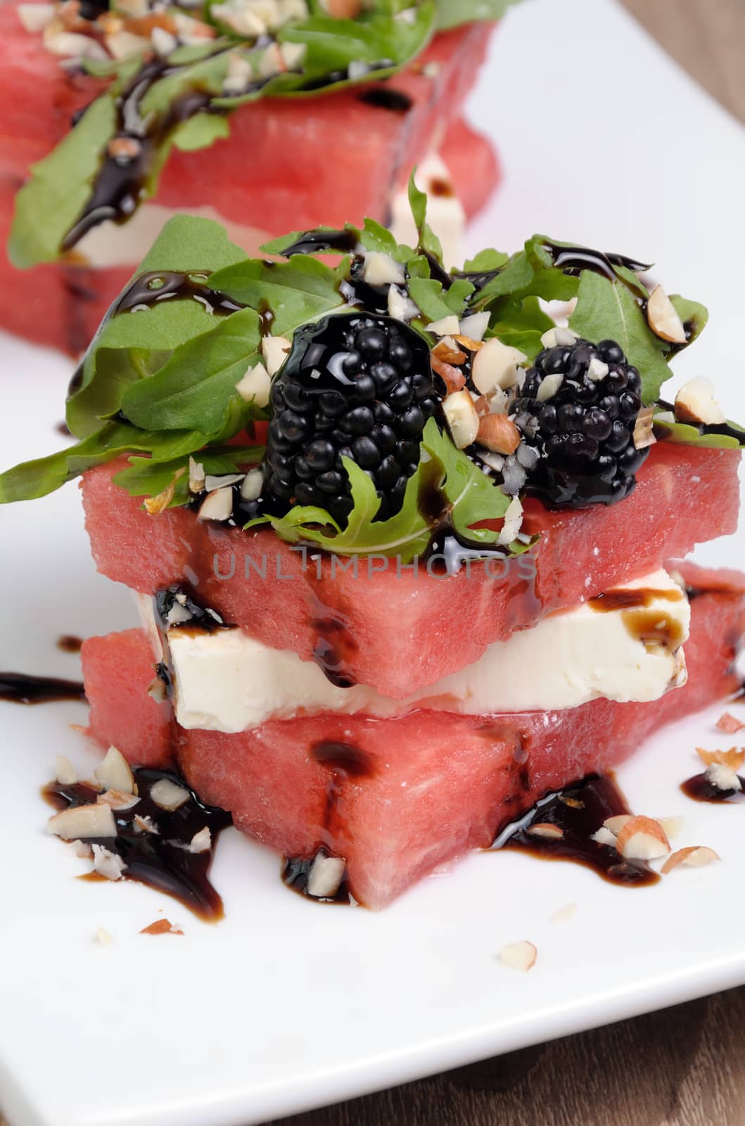 appetizer  stacked slices of watermelon, feta, arugula, blackberry sauce and nuts