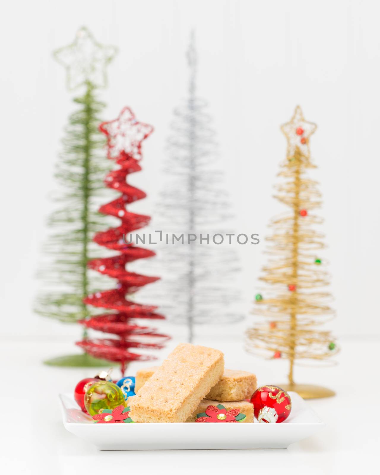 Plate of traditional festive shortbread cookies with christmas trees in the background.