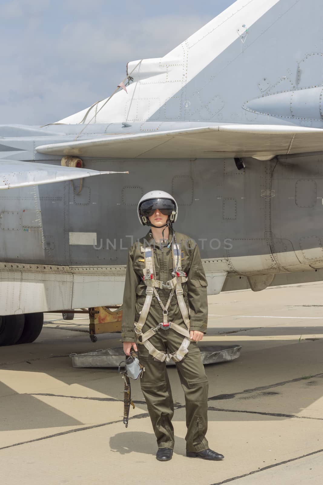 Military pilot in helmet stands near jet plane.