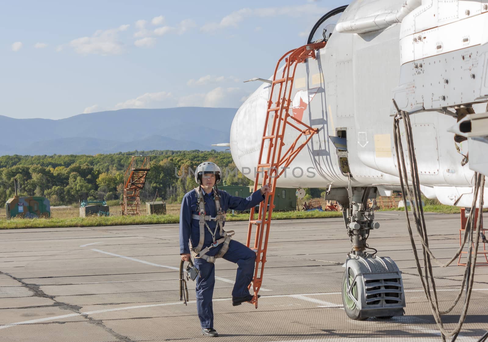 Military pilot in helmet stands near jet plane.