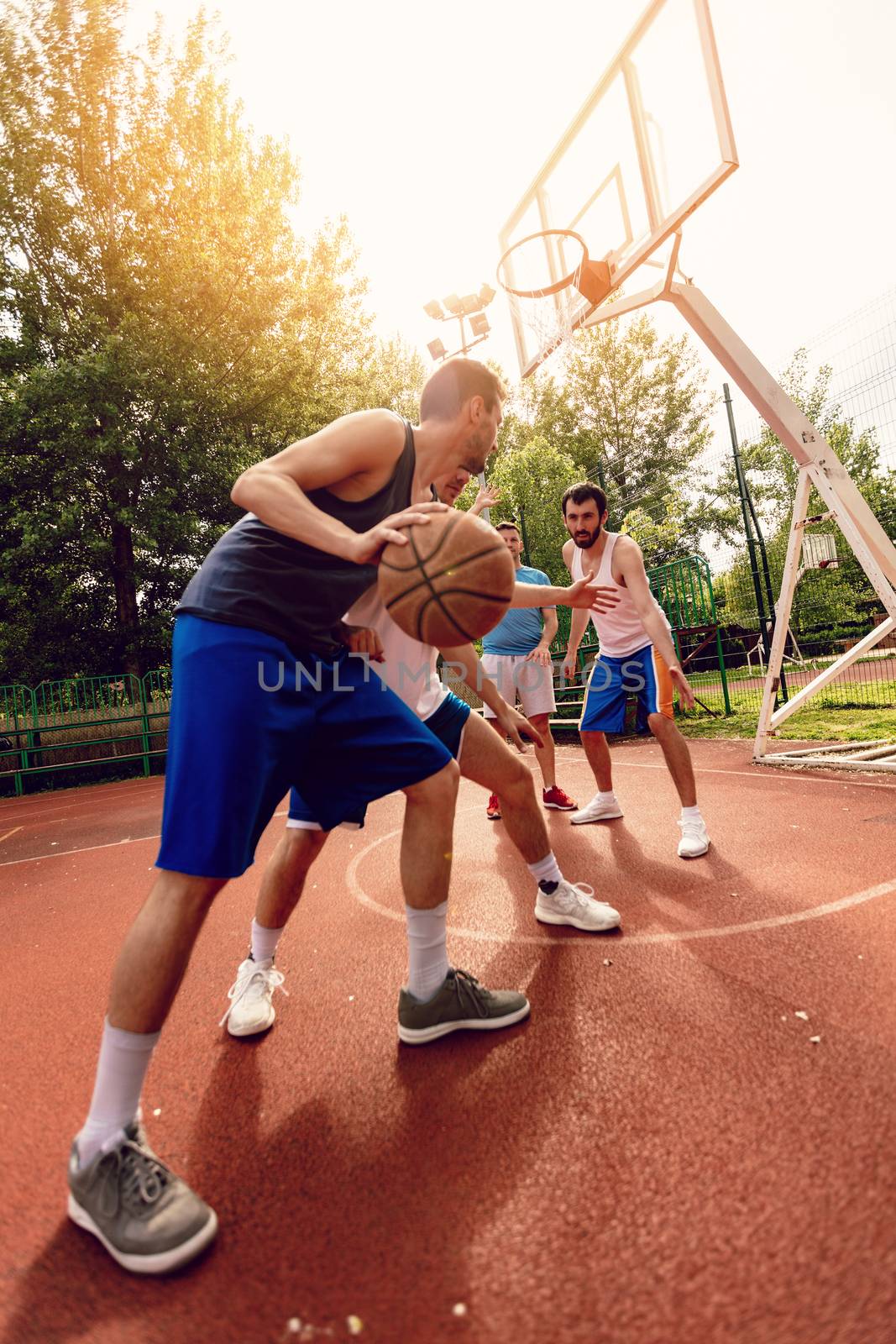 Four basketball players have a training outdoor. They are playing and making action together.