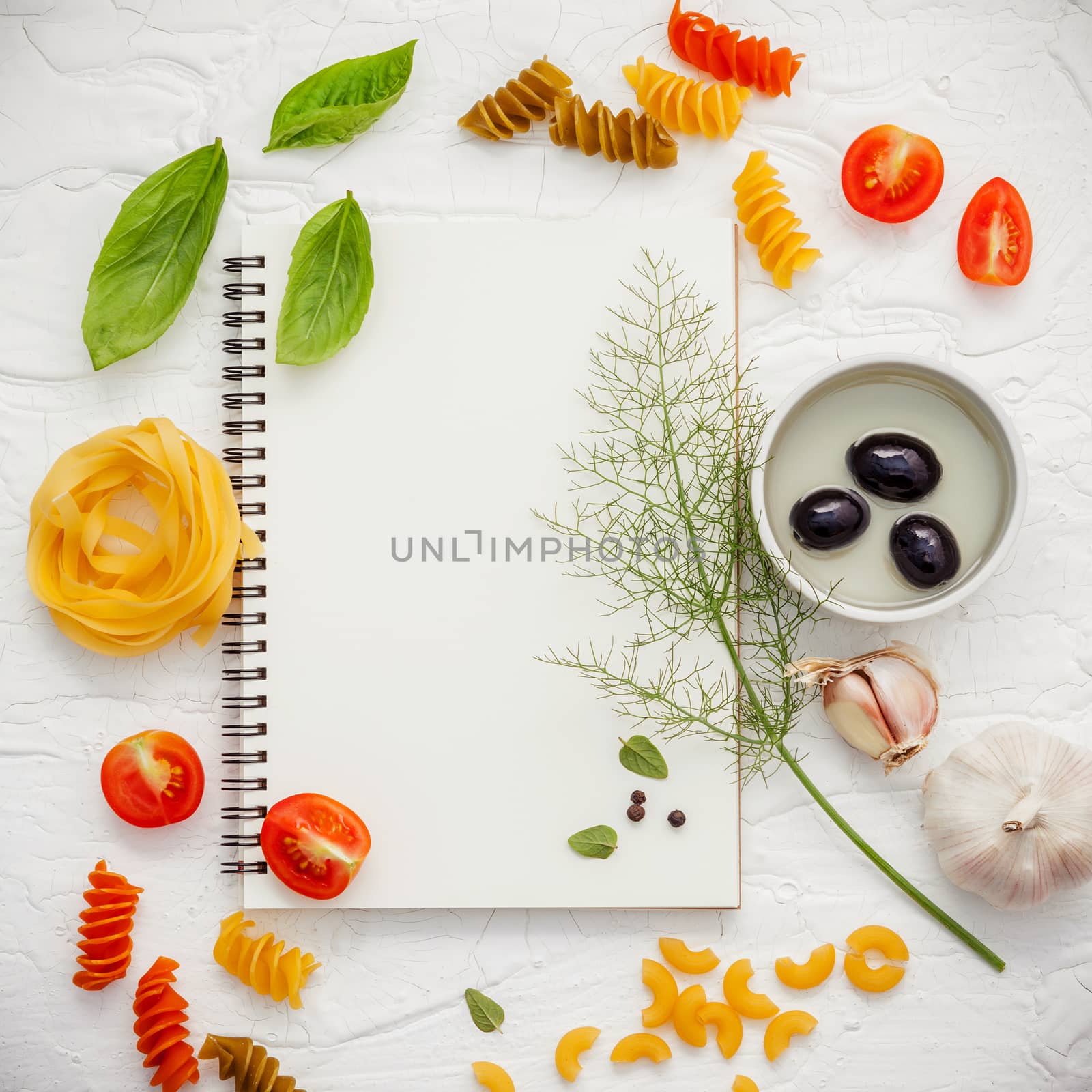 Italian foods concept and menu design . Various pasta elbow macaroni ,fusilli ,fettucini with ingredients sweet basil, sage ,black olive ,himalayan salt ,pepper and garlic setup on white notebook .