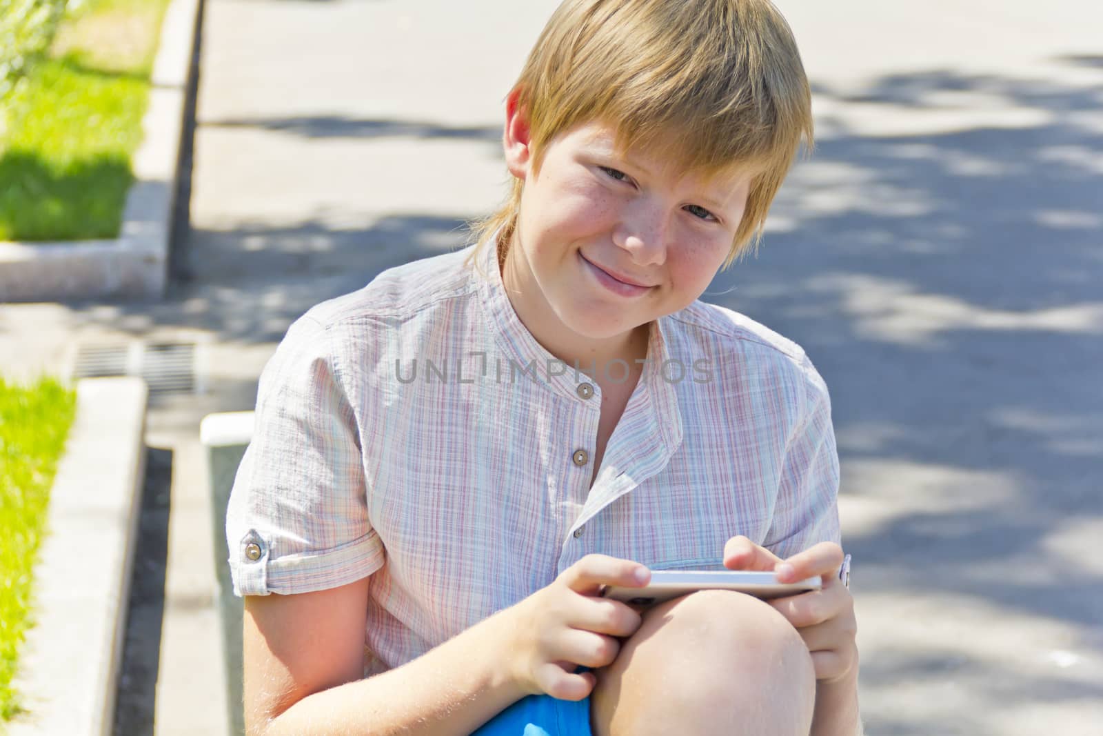 Blonde smiling boy with cellular phone in summer
