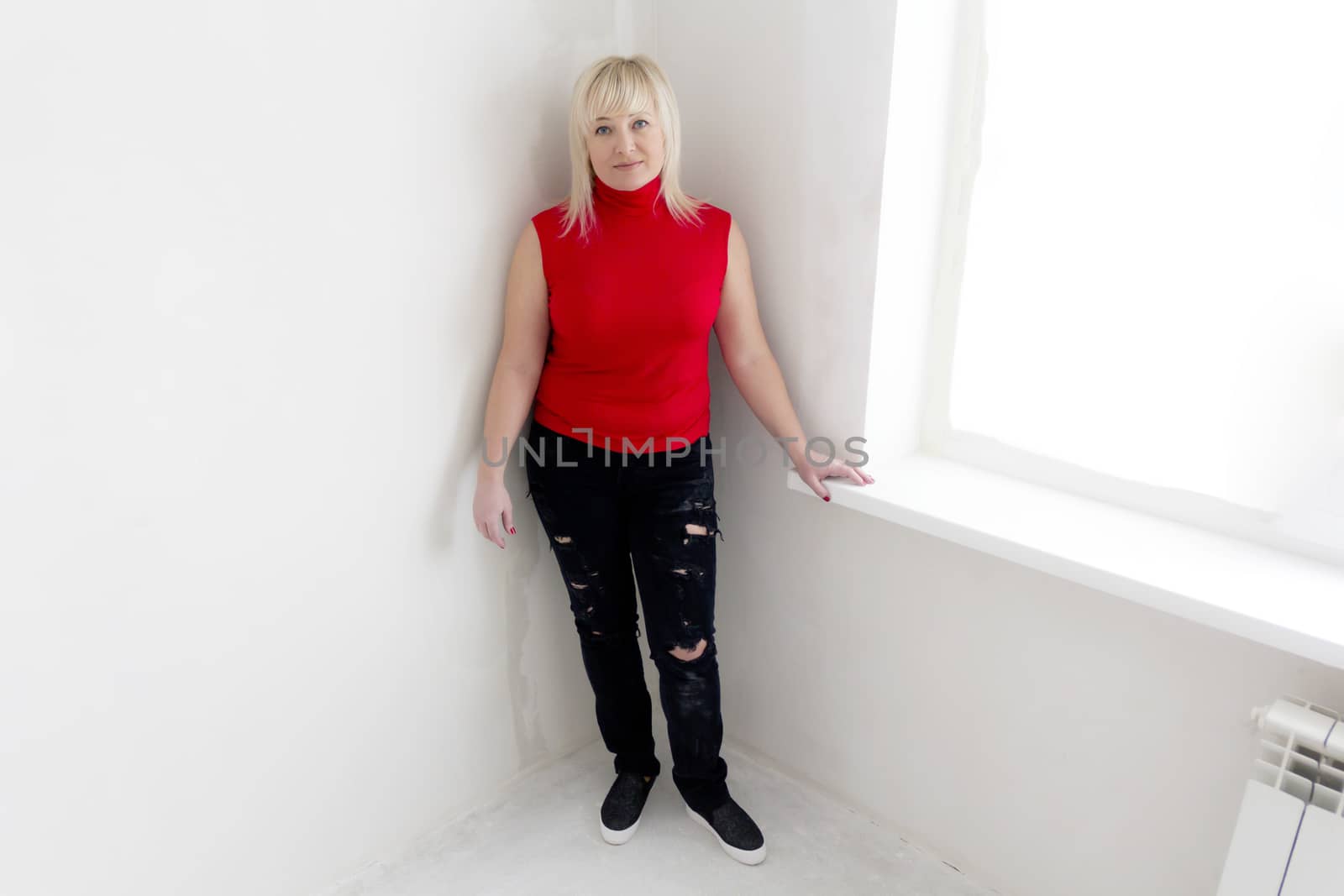 Blond woman in red and black jeans stand inside empty room