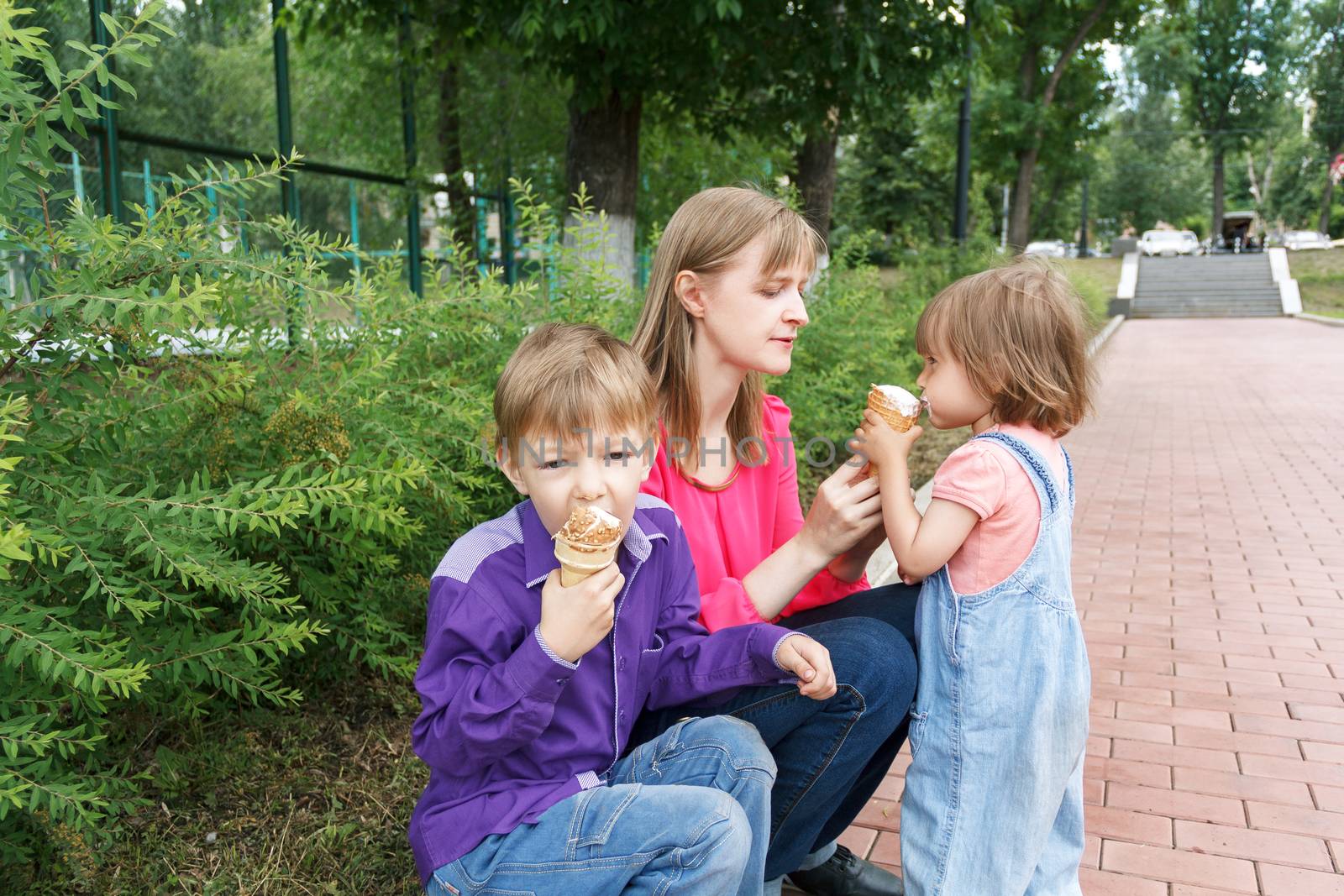 Mother with boy and baby girl sitting in summer park eating icecream