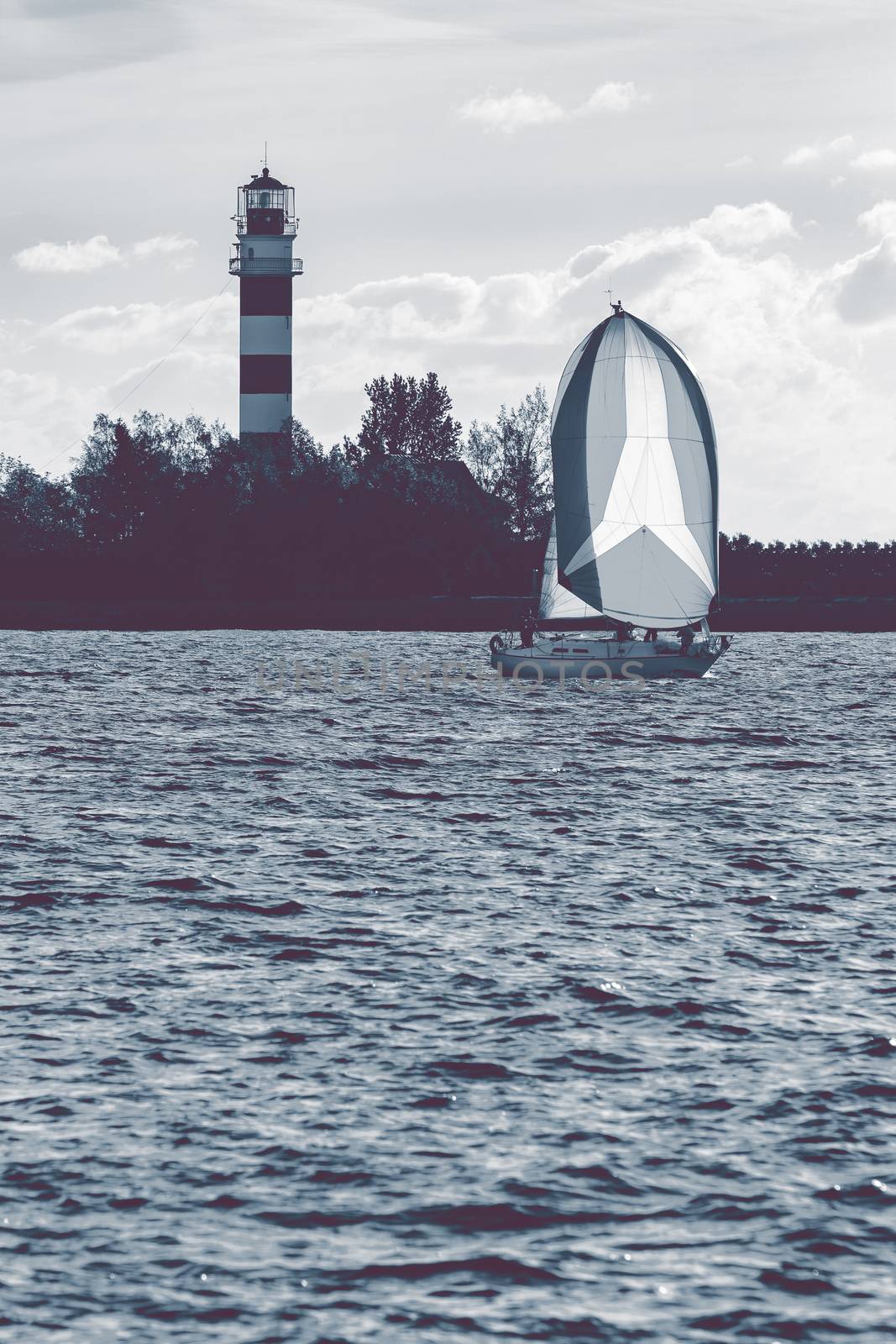 Sailboat sailing past the big lighthouse in evening, Latvia