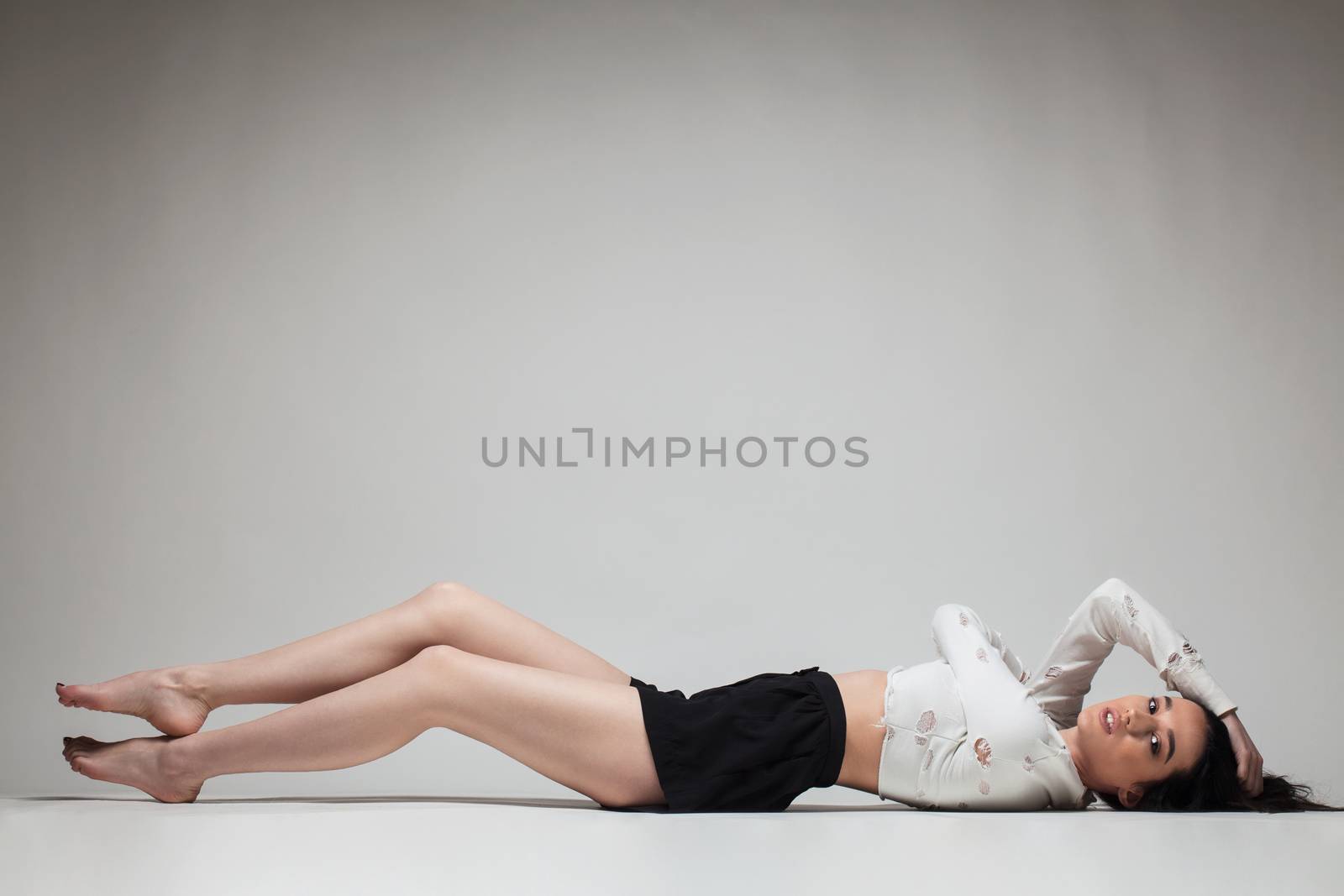 full body shot of beautiful black haired lady lying on the ground bare feet