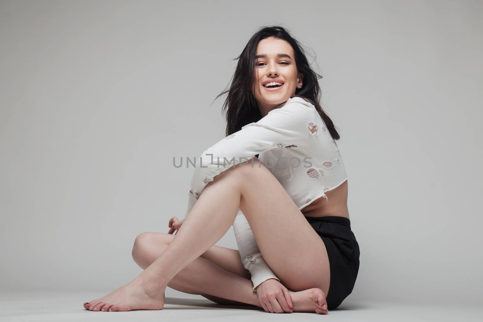 full body shot of beautiful black haired lady sitting on the ground bare feet