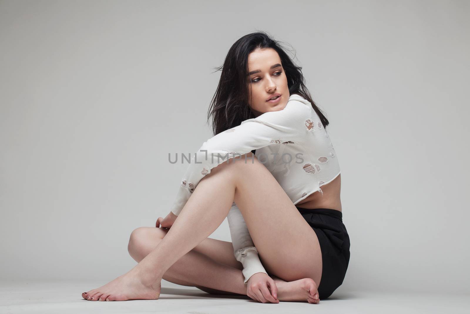 full body shot of beautiful black haired lady sitting on the ground bare feet