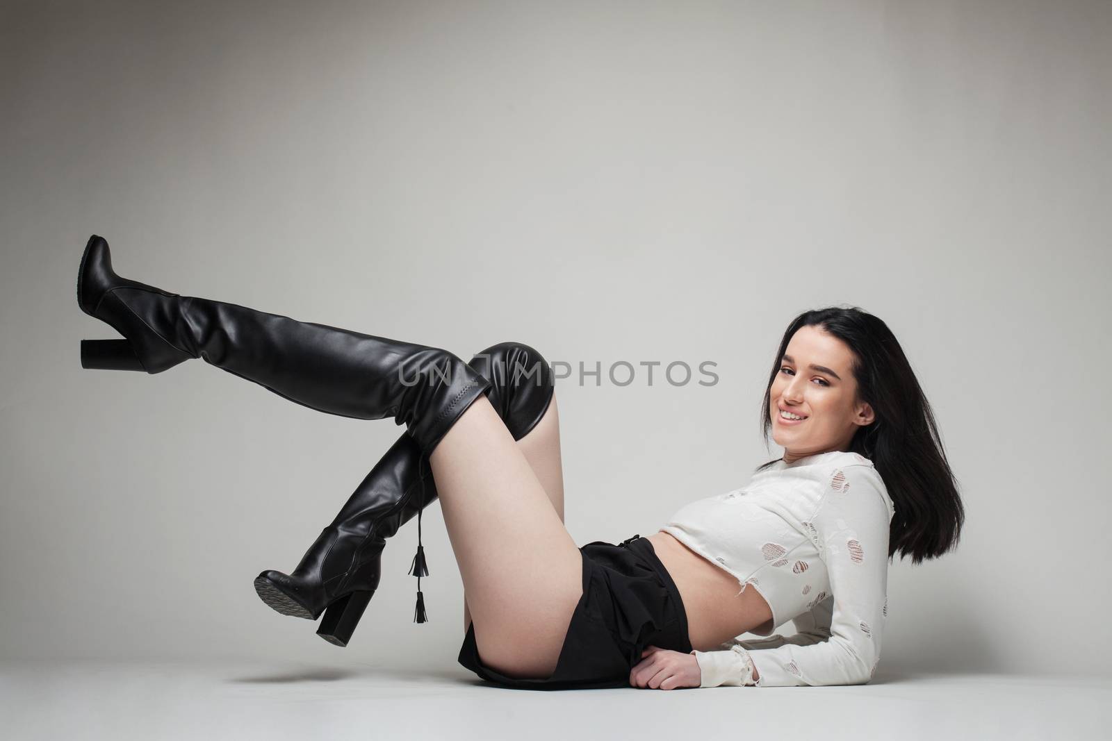 full body shot of beautiful black haired lady wearing high heels boots, sitting on the ground