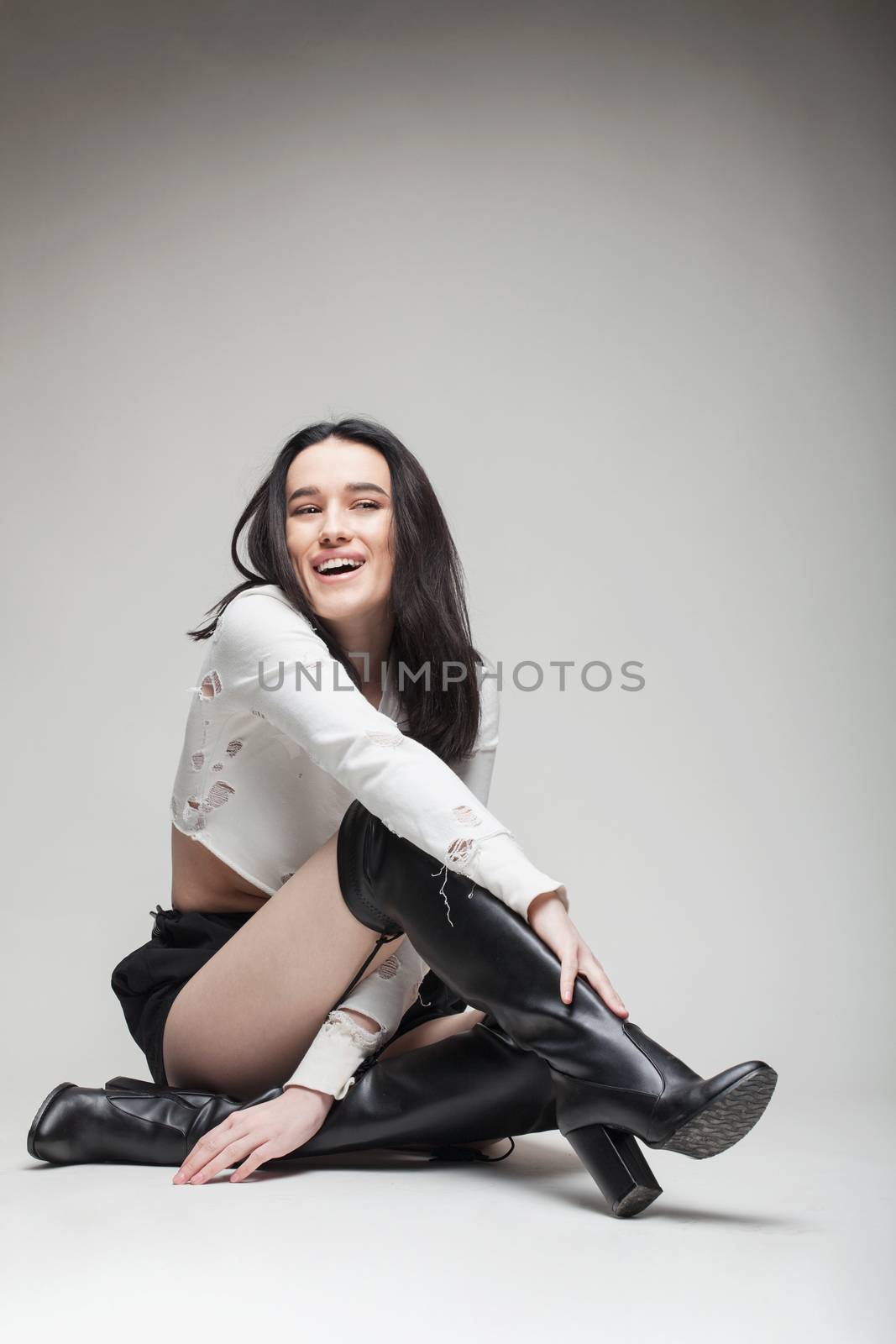 full body shot of beautiful black haired lady wearing high heels boots, sitting on the ground
