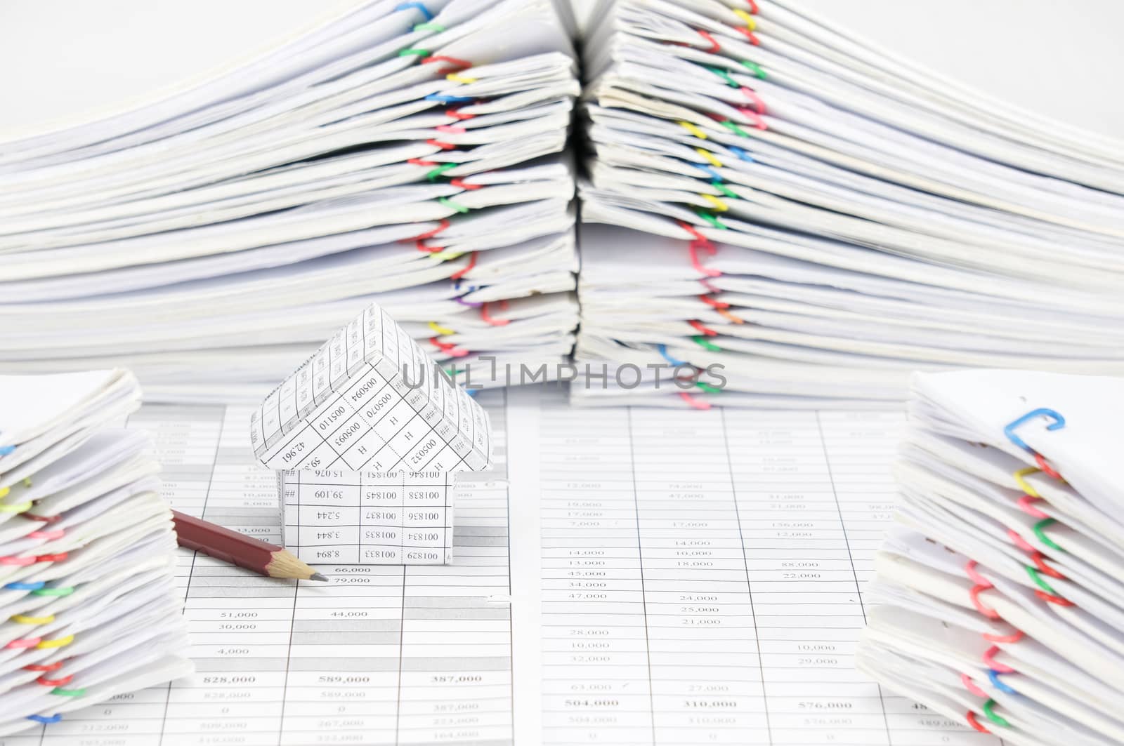 House and pencil on finance account have blur pile overload document of report and receipt with colorful paperclip as foreground and background.