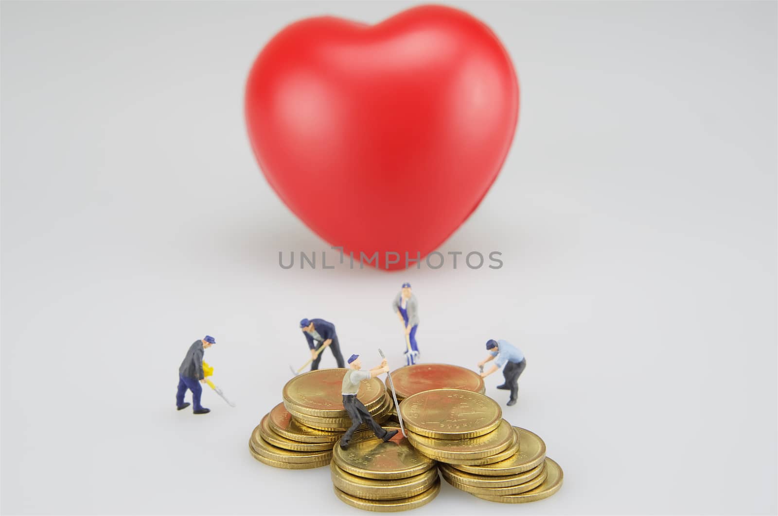 Coin stacks with miniature and blur red heart on white background.