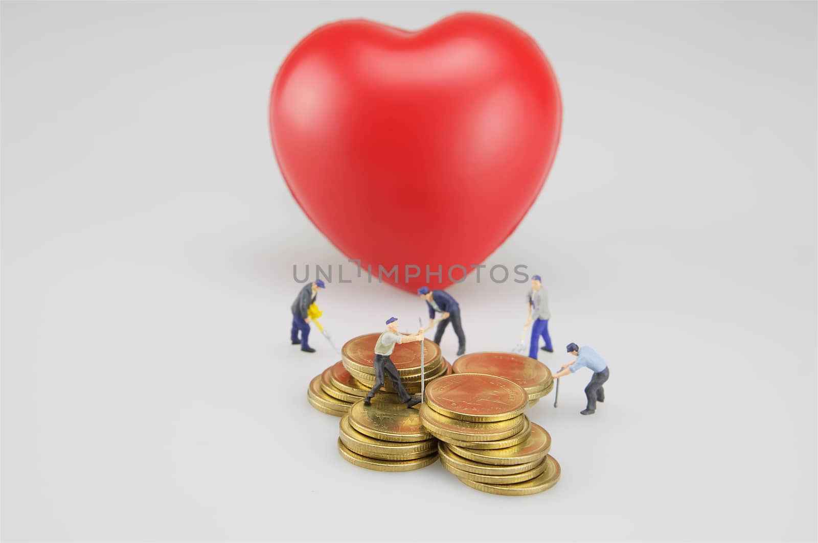Coin stacks with miniature and red heart on white background.