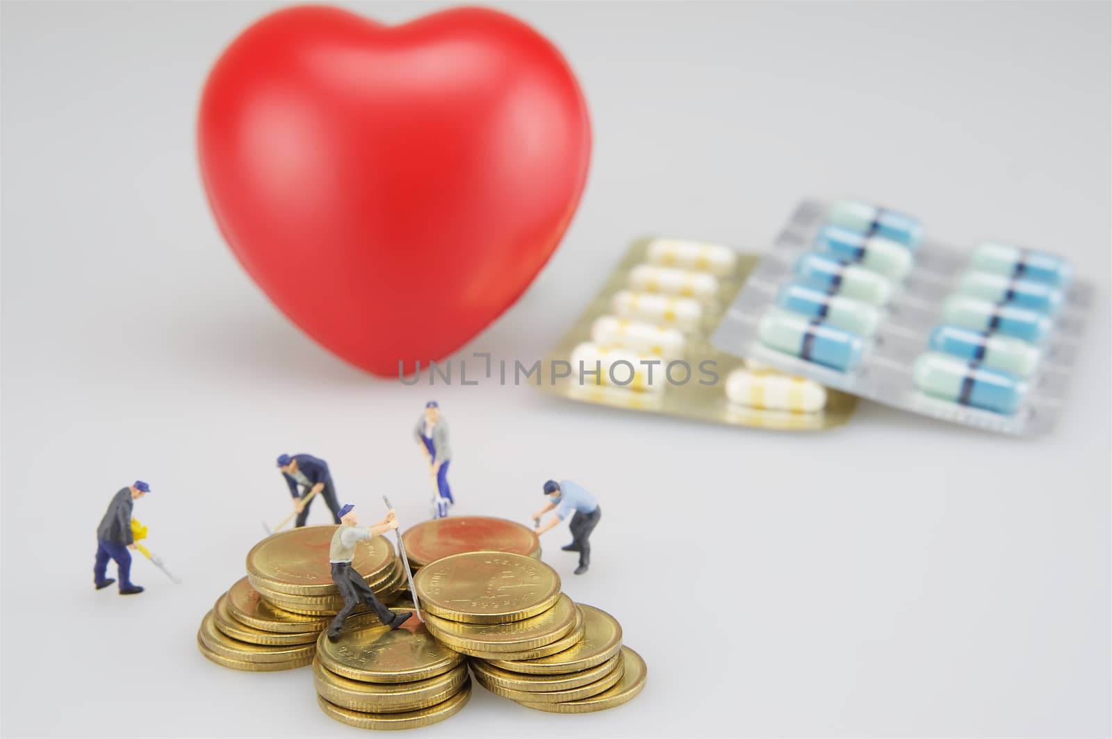 Pile of coins with miniature people, packing of medicine and red heart.
