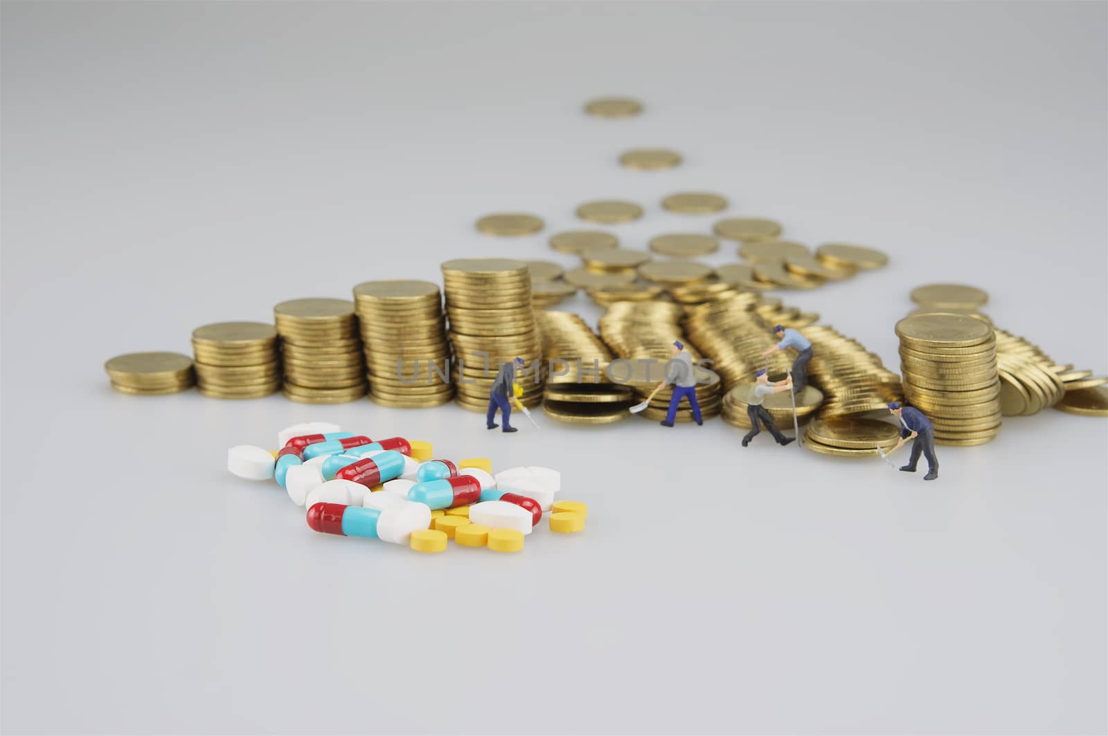 Stack of gold coin with miniature people and medicine on white background.