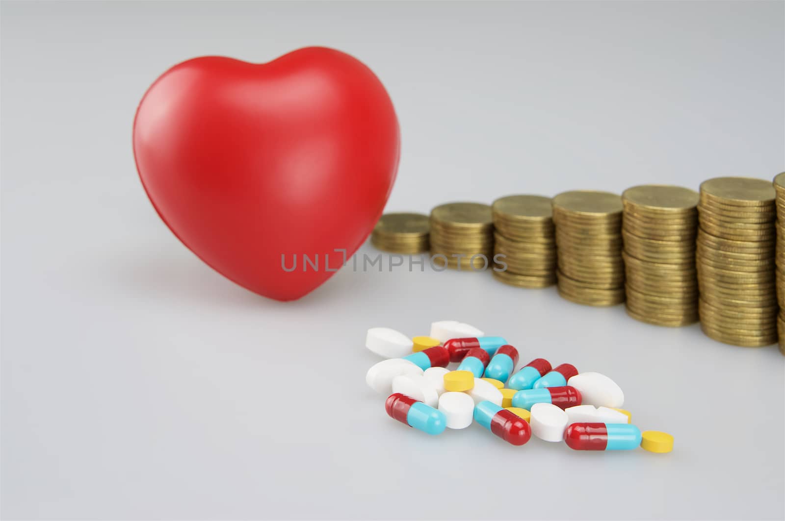 Stack of medicine and red heart with gold coins on white background.