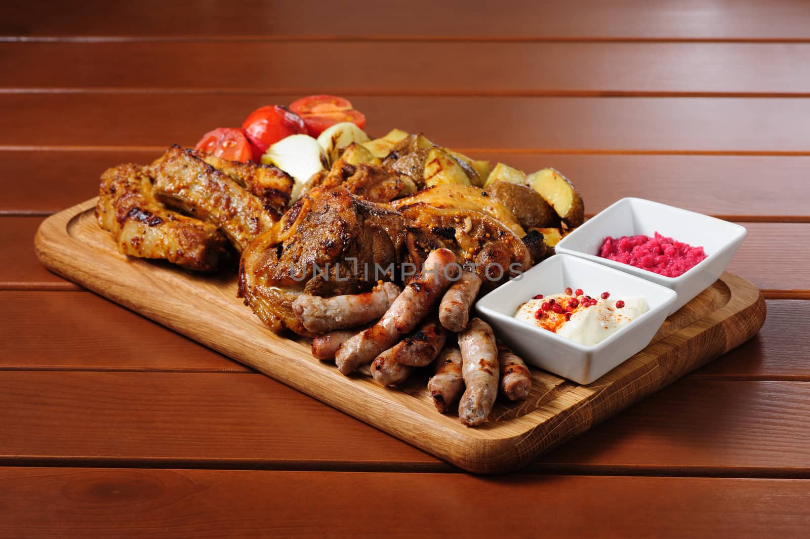 big wooden board with pork ribs and steaks baked in mustard sauce, small sausages, baked potato, grilled tomatoes and onion, hot sauce and horseraddish sauce, preferably served as companion for beer or other alcohol drinks