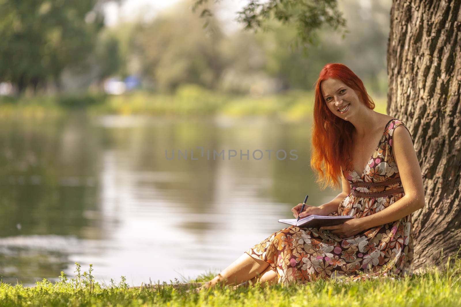 Young redhead woman writing in summer park