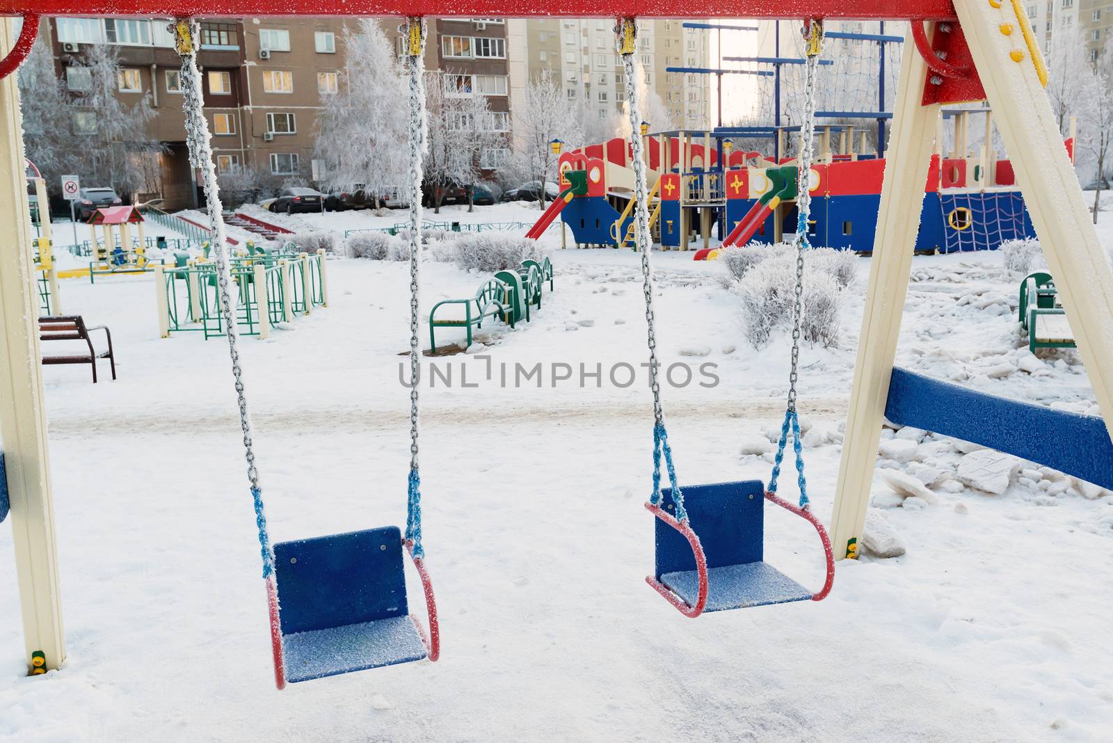 snow covered swing and slide at playground in winter by olgavolodina