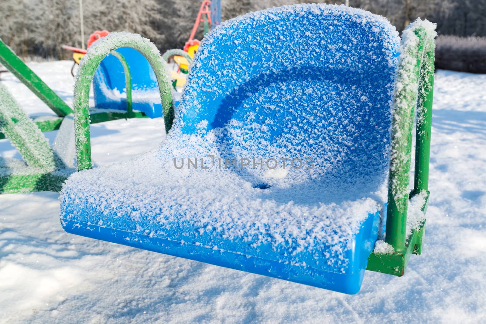 snow covered swing and slide at playground in winter by olgavolodina