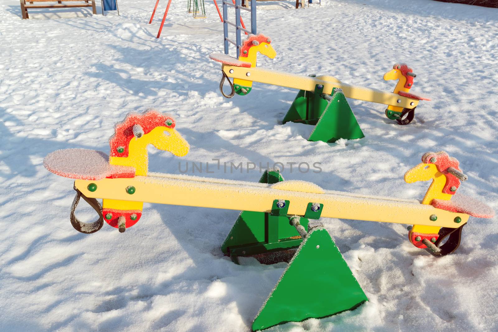 snow covered swing and slide at playground in winter by olgavolodina