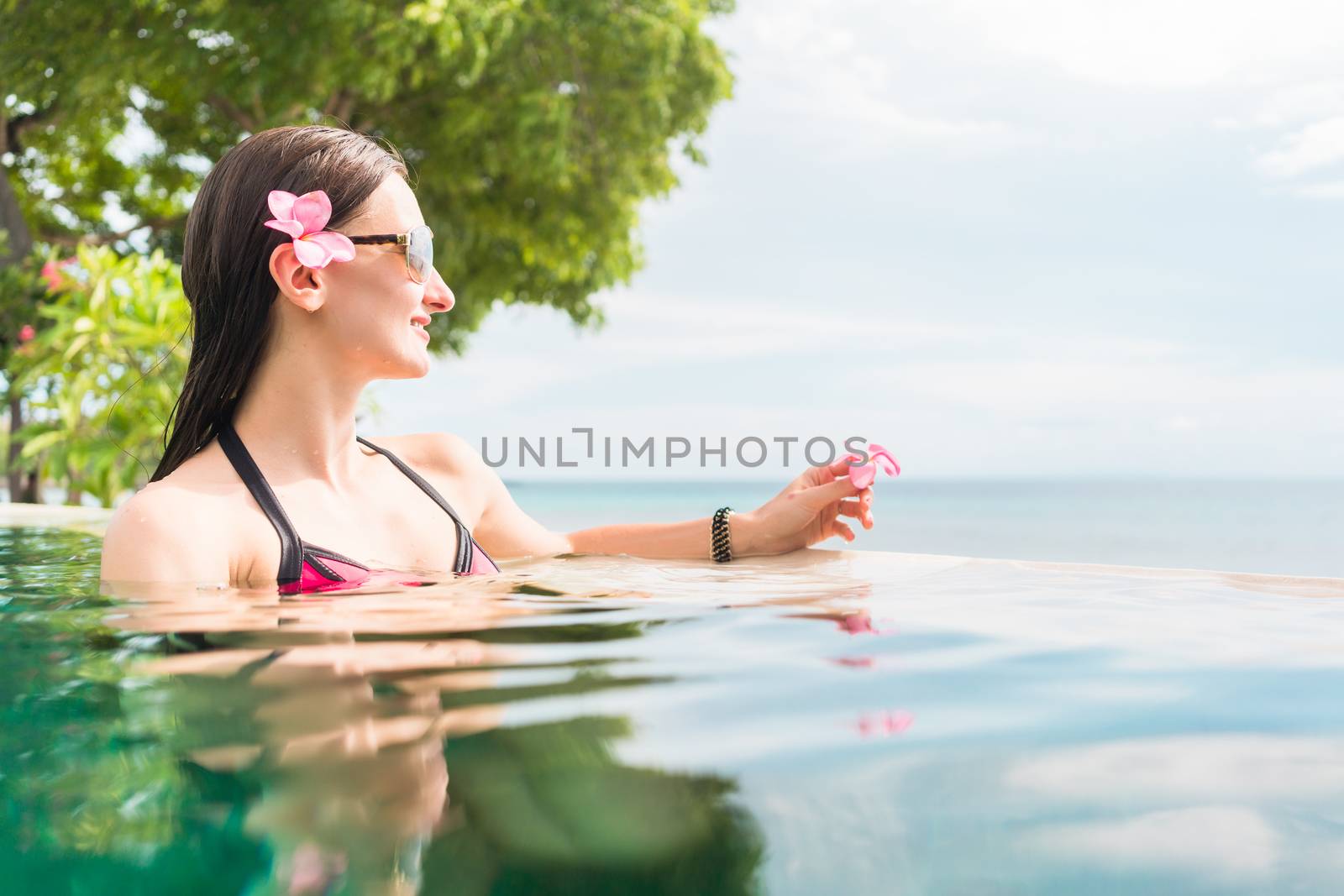 Woman in summer vacation relaxing swimming in pool with the ocean in the background