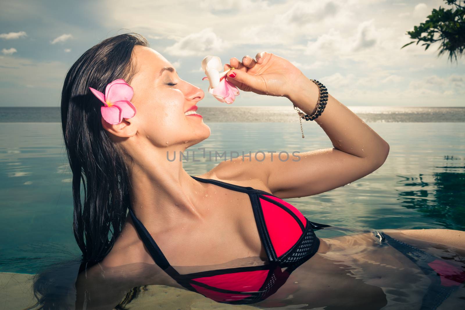 Woman Tourist in infinity pool of hotel resort showing pink blossom of frangipani flower