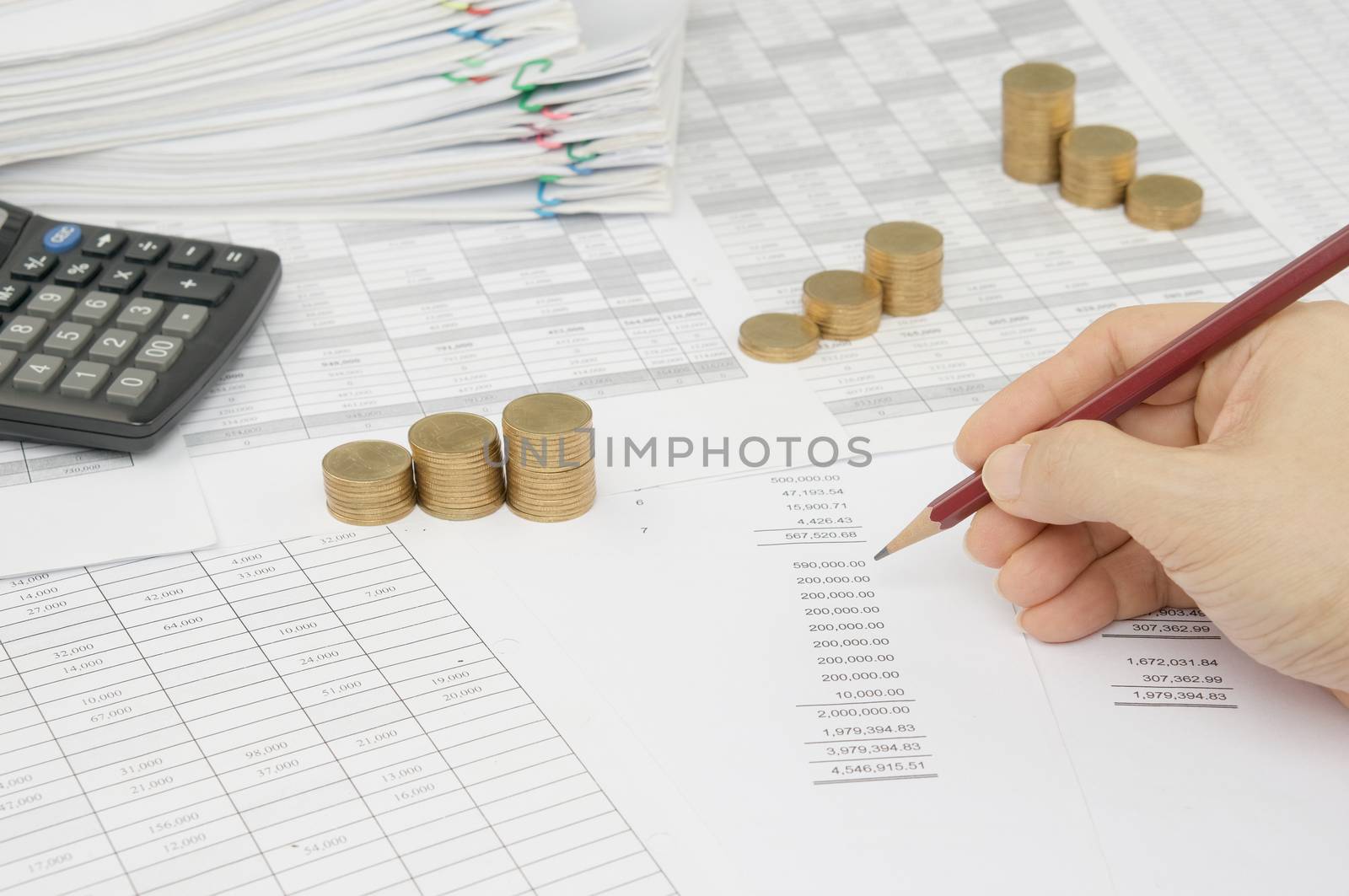 Man is auditing account by pencil with step pile of gold coins on the statement finance account have blur calculator and overload of paperwork with colorful paperclip as background.