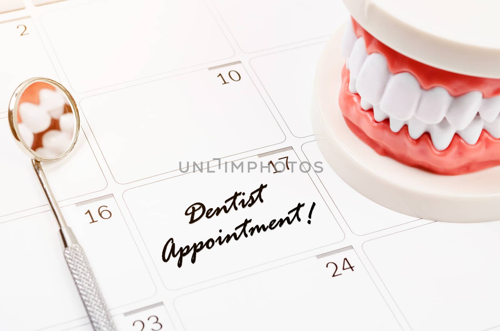 Dentist appointment word on calendar page and Dentist mirror tool and dentist demonstration teeth model.
